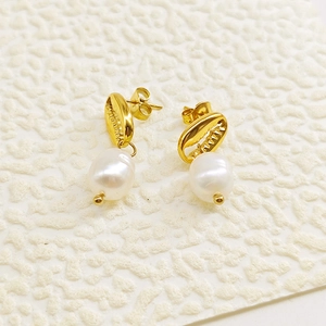 Détail de boucles d'oreilles coquillage dorées avec perles blanches sur fond texturé