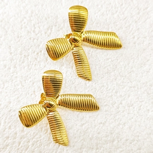 Macro detail of 18k gold plated bow stud earrings featuring ribbed metal texture