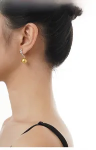 Detailed view of elegant gold pearl drop earrings with silver hooks on a female model