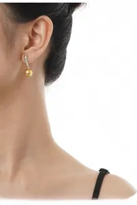 Close-up of a golden round pearl earring on model with sparkling silver hooks