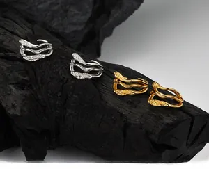 Macro detail of irregular fluid metal ear cuffs in silver and gold on charcoal wood