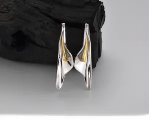 Macro shot of silver Calla Lily earrings with golden pistils on dark textured wood