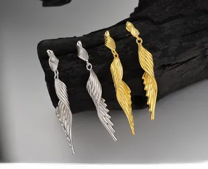 Detail view of long tassel wing earrings in silver and gold finish on charcoal