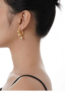 Detailed shot of gold C-shaped earrings featuring natural lava texture and white pearls