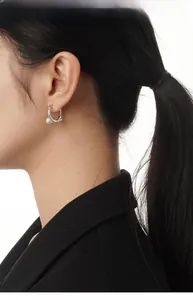 Detail shot of a silver hoop earring with a white pearl on a model in black attire