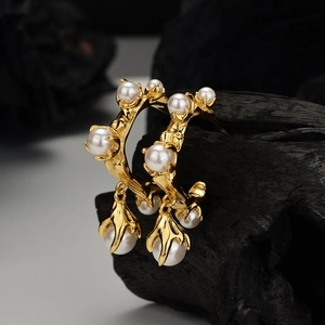 Artistic gold flower C-shaped earrings with baroque pearls on a charcoal background