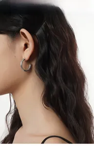 Gros plan sur des créoles argentées en C avec motifs vintage gravés portées par un mannequin