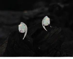 Macro shot of silver crescent moon opal earrings with sparkling crystal accents on coal