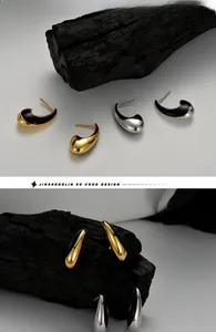 Close-up of S925 silver crescent stud earrings with black enamel on charcoal background