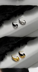 Close-up of minimalist teardrop earrings in gold and silver with black enamel inlay