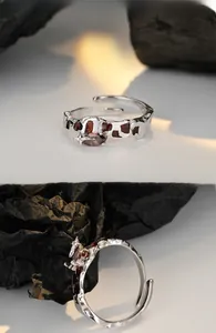 Dettaglio anello argento in metallo liquido con gemme rosso scuro su carta strutturata