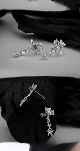 Macro detail of irregular silver cross earrings with light blue gemstone in gothic style