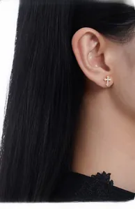 Close-up of gold cross stud earrings with cubic zirconia worn by a model on white background
