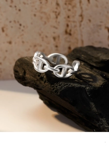 Macro detail of silver anchor link ring with matte brushed finish on charred wood