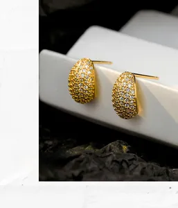 Macro shot of gold teardrop earrings with pave-set sparkling zircon on black stone