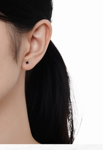 Close-up of a minimalist black star stud earring worn on ear with clean white background