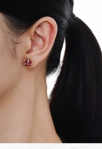 Detailed close-up of a red enamel snake and apple earring on a model ear lobe