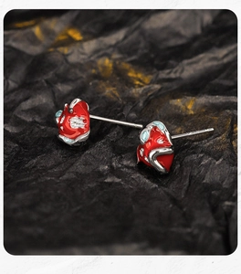 Macro shot of 925 silver red enamel snake wrapping apple earrings on black textured paper