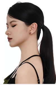 Close-up of a red enamel snake and apple earring worn by a model against a white background