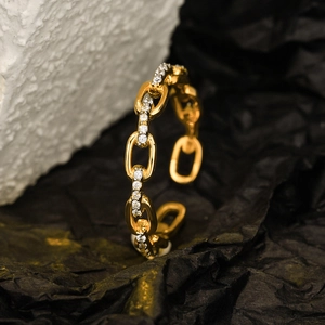 Minimalist gold chain link ring with sparkling crystals on black and white stone background