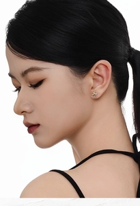 Détail d'un clou d'oreille croix en argent S925 avec un petit cœur doré sur l'oreille