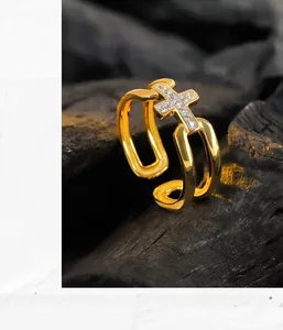 Détail d'une bague croix dorée à double couche avec cristaux sur un support texturé