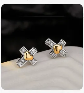 Détail macro de boucles d'oreilles X en argent avec pierres et cœur doré au centre