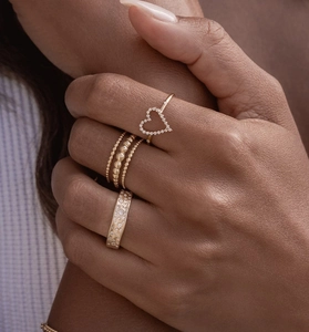 Detailed close-up of a stack of three gold rings including a hollow heart and beaded band