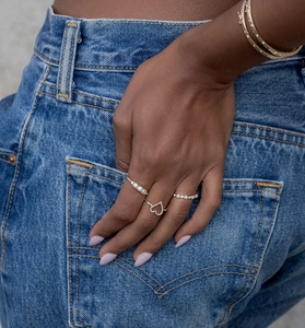 Detail of stacked S925 silver heart rings and gold bangles with pearls on denim background