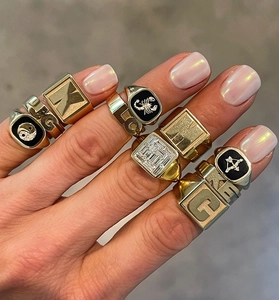 Close-up of layered gold rings with initials, zodiac signs and square cubic zirconia stones