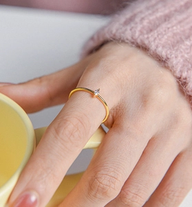 Detail of a minimalist gold ring with a marquise-cut zircon on a model holding a cup