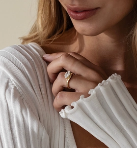 Detailed view of a marquise-cut gemstone gold ring on model wearing a white knit sweater