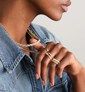 Close-up of model wearing gold tiered rings and layered necklaces with denim shirt
