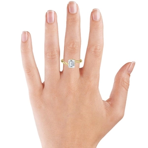 Elegant emerald cut solitaire ring with gold crossover band on finger