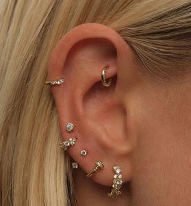 Macro shot of stacking gold S925 silver earrings set with sparkling zircon on ear