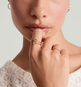 Detailed view of layered spiral gold-plated ring with round zircon stones on model hand