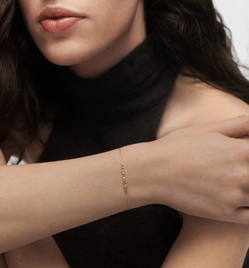 Detail of a thin gold chain bracelet with colorful mini gemstones on a wrist