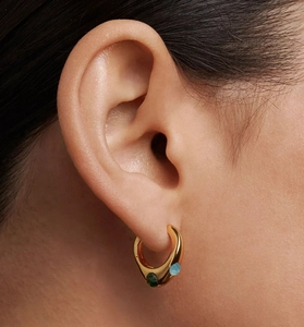 Close-up of gold irregular hoop earring with green and blue zircon gemstones on model