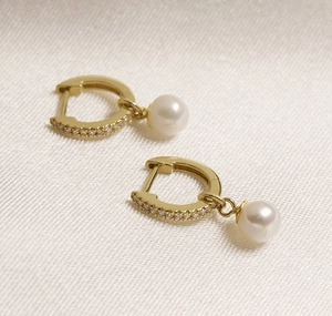 Close-up of gold-plated hoop earrings featuring pavé diamonds and lustrous white pearls