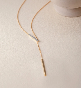 Macro view of gold geometric pendant necklace with pavé zircons and polished metal bar