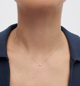 Gros plan d'un collier solitaire doré avec un zircon blanc rond porté par un mannequin