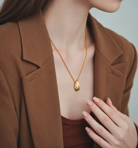 Detail of a textured golden teardrop pendant with molten metal finish on a slim chain