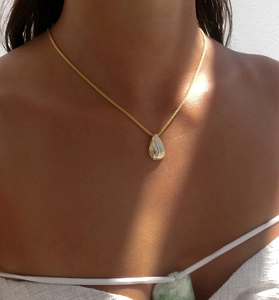 Detail of gold water-drop pendant featuring brushed texture and polished finish on a chain