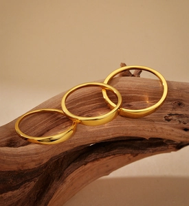 Close-up of three minimalist polished gold rings stacked on a piece of natural wood