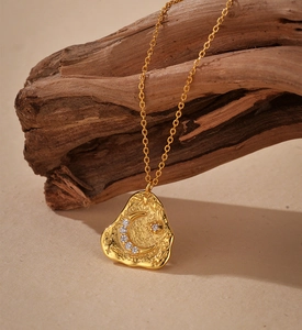 Detail of moon and star gold pendant with textured surface hanging on wood