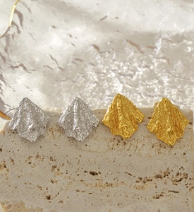 Gros plan de boucles d'oreilles froissées dorées et argentées sur pierre claire