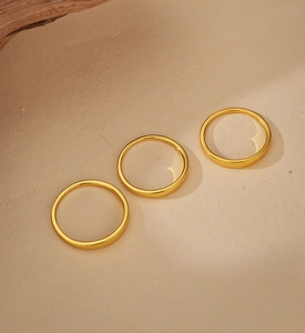 Detailed view of three minimalist polished gold rings on a textured sandy background