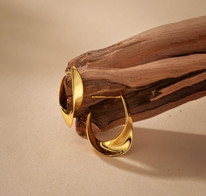 Detailed close-up of golden twisted ribbon earrings on natural textured wood