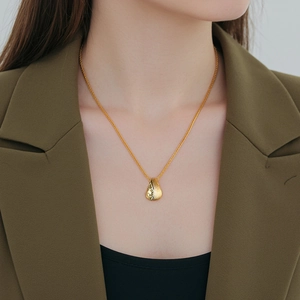 Elegant gold drop pendant necklace with brushed texture on model in green blazer