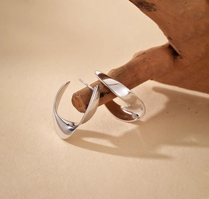 Detail of silver twisted C-shape earrings displayed on a natural wooden stand